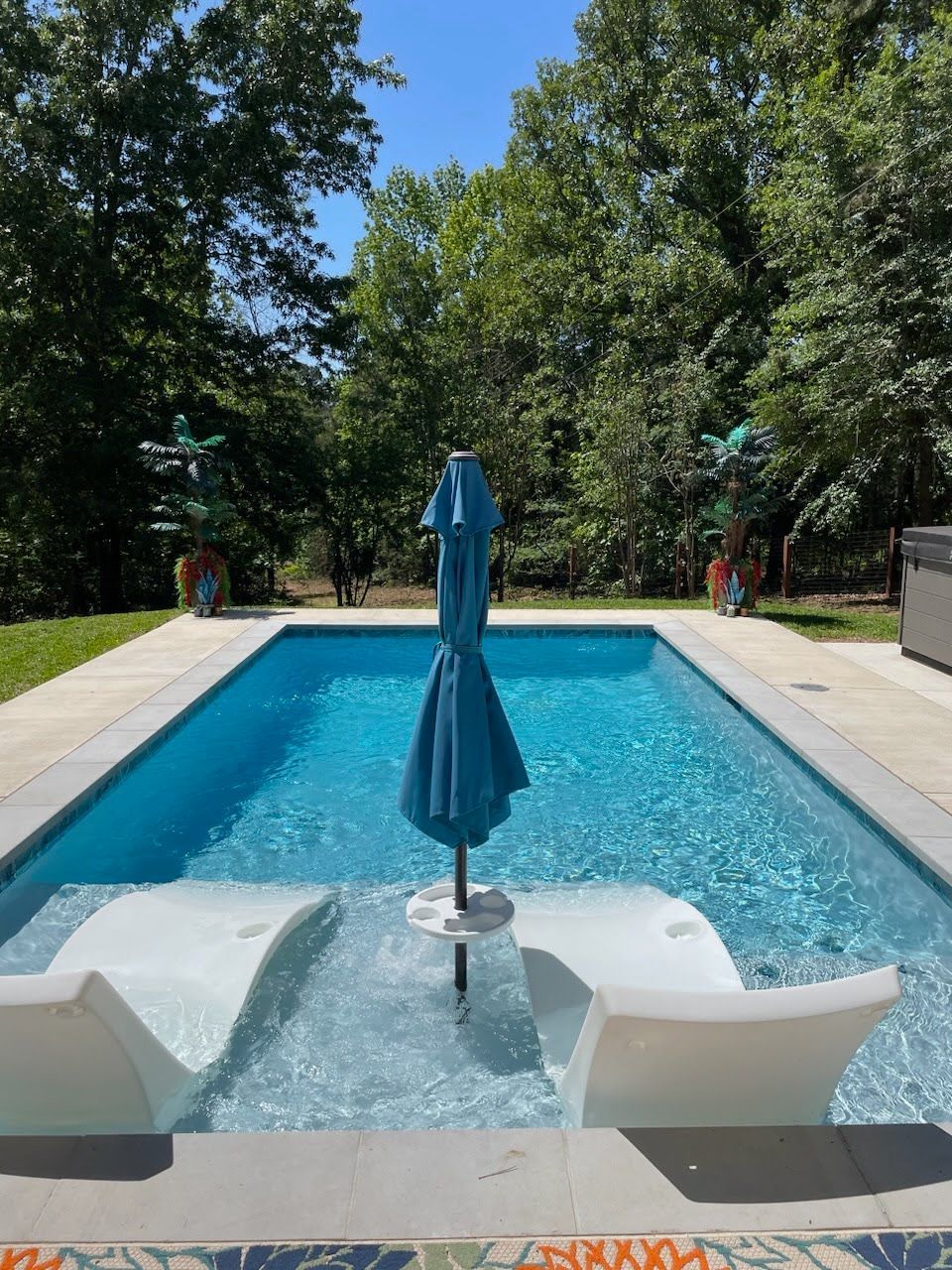 A large swimming pool with a blue umbrella in the middle.