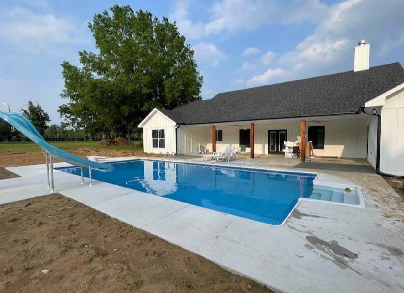 A large swimming pool is in the backyard of a house.