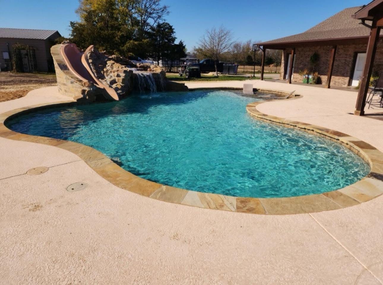 A large swimming pool with a waterfall in the backyard of a house.