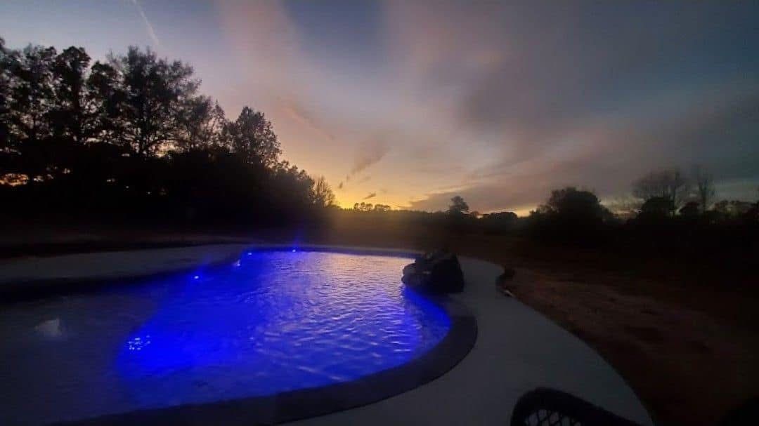 A swimming pool is lit up with blue lights at sunset.