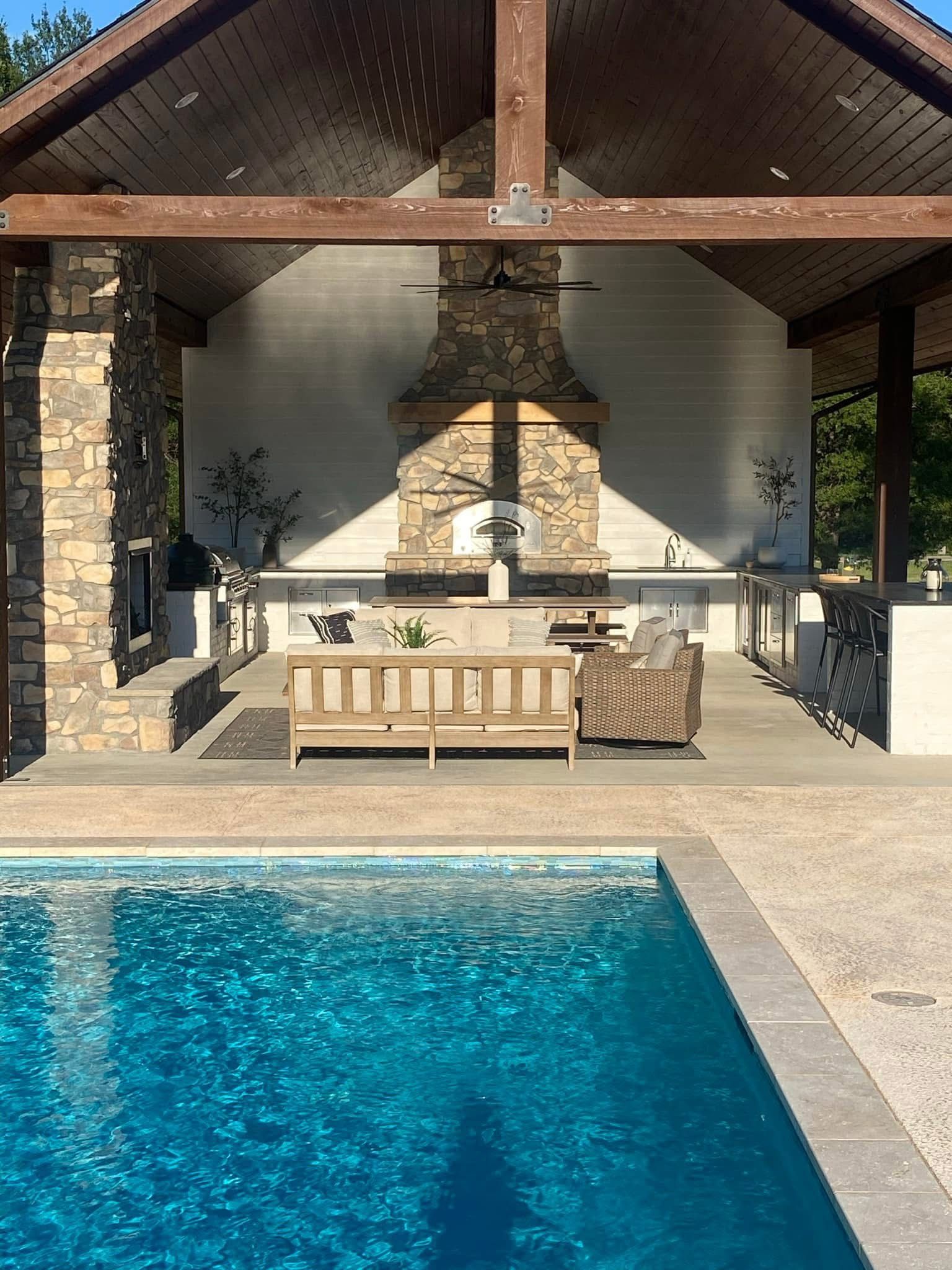 A large swimming pool is surrounded by a covered patio area with a fireplace.