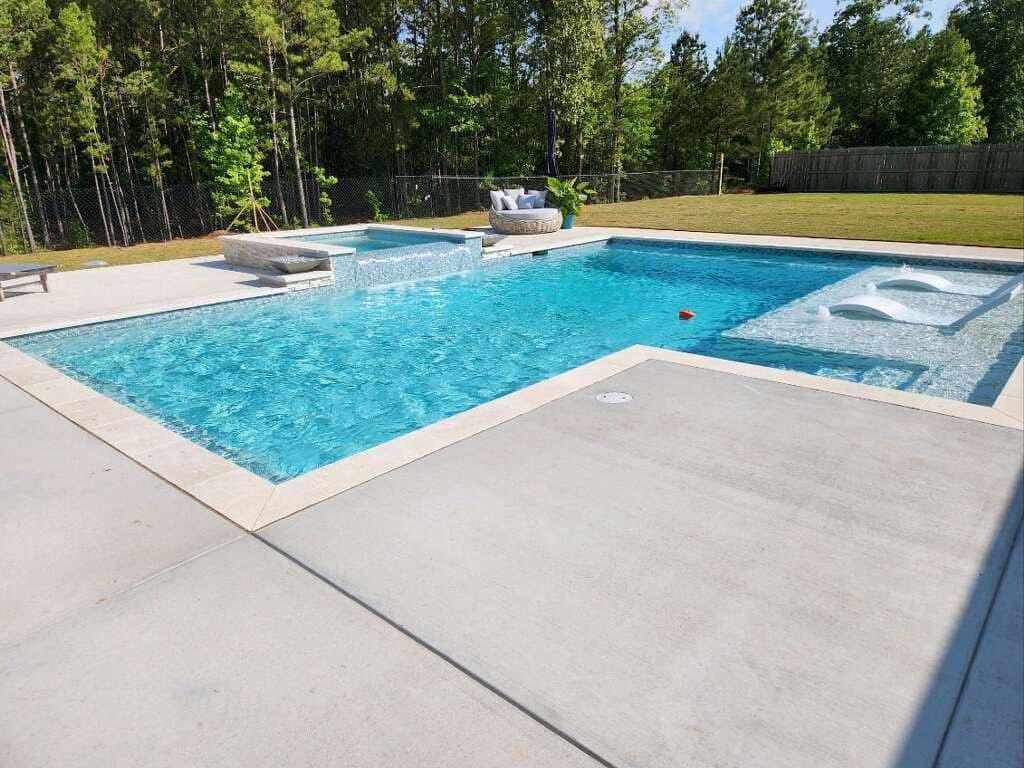 A large swimming pool is surrounded by trees and a concrete patio.