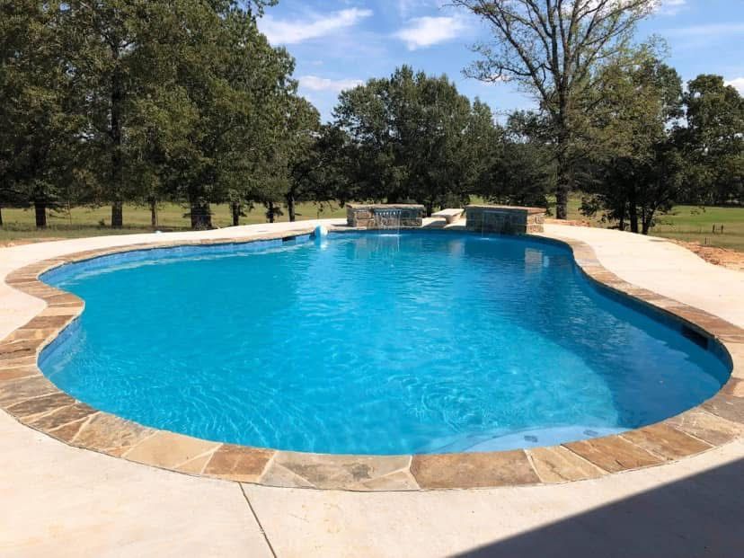 A large swimming pool surrounded by trees on a sunny day.