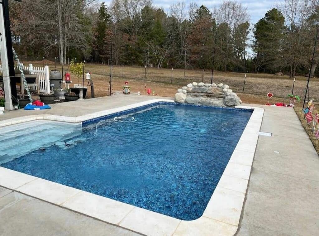 A large swimming pool is surrounded by trees and a patio.
