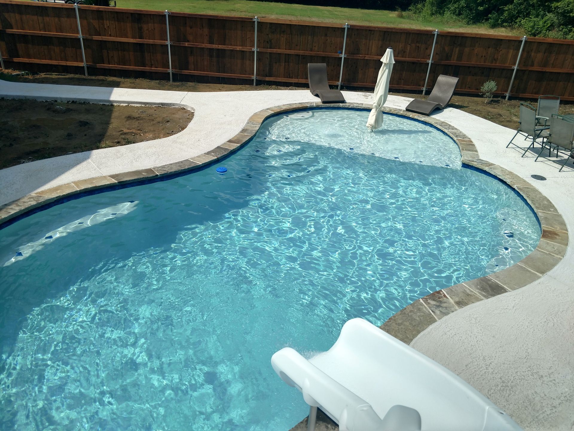 A large swimming pool with a slide and chairs around it.