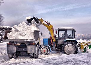A tractor is loading snow into a dump truck