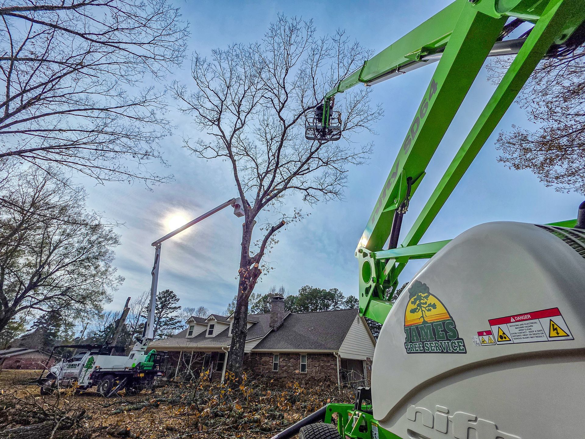 A lime-green cherry picker parked in a yard with a tree being trimmed above a house.