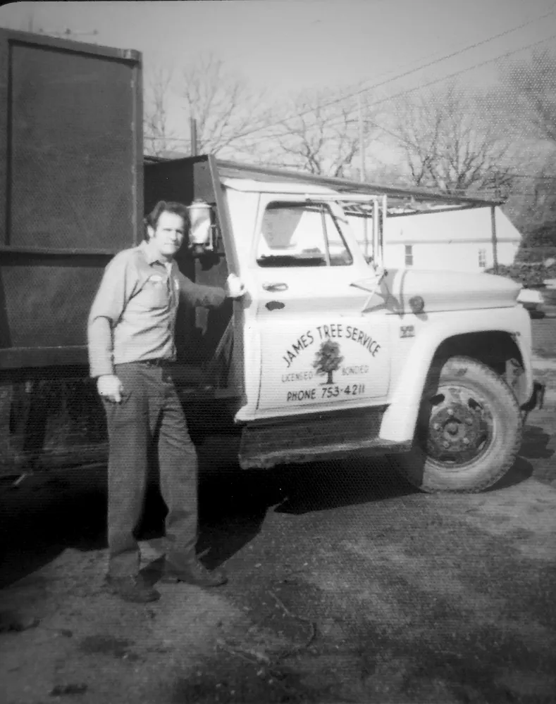 Man standing next to his tree service truck with the business name and phone number on the side.
