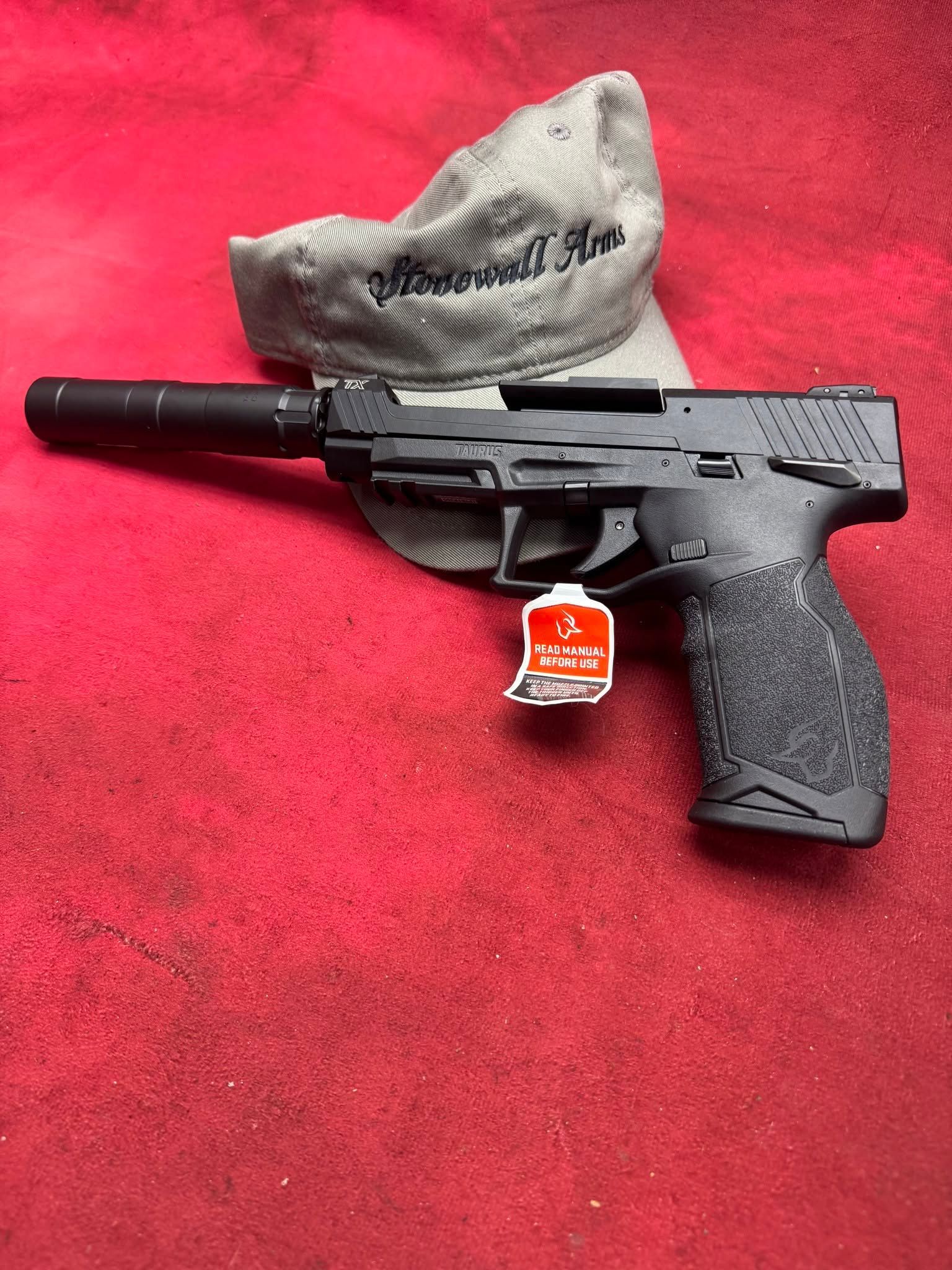 Black handgun with suppressor and gray cap on a red surface.