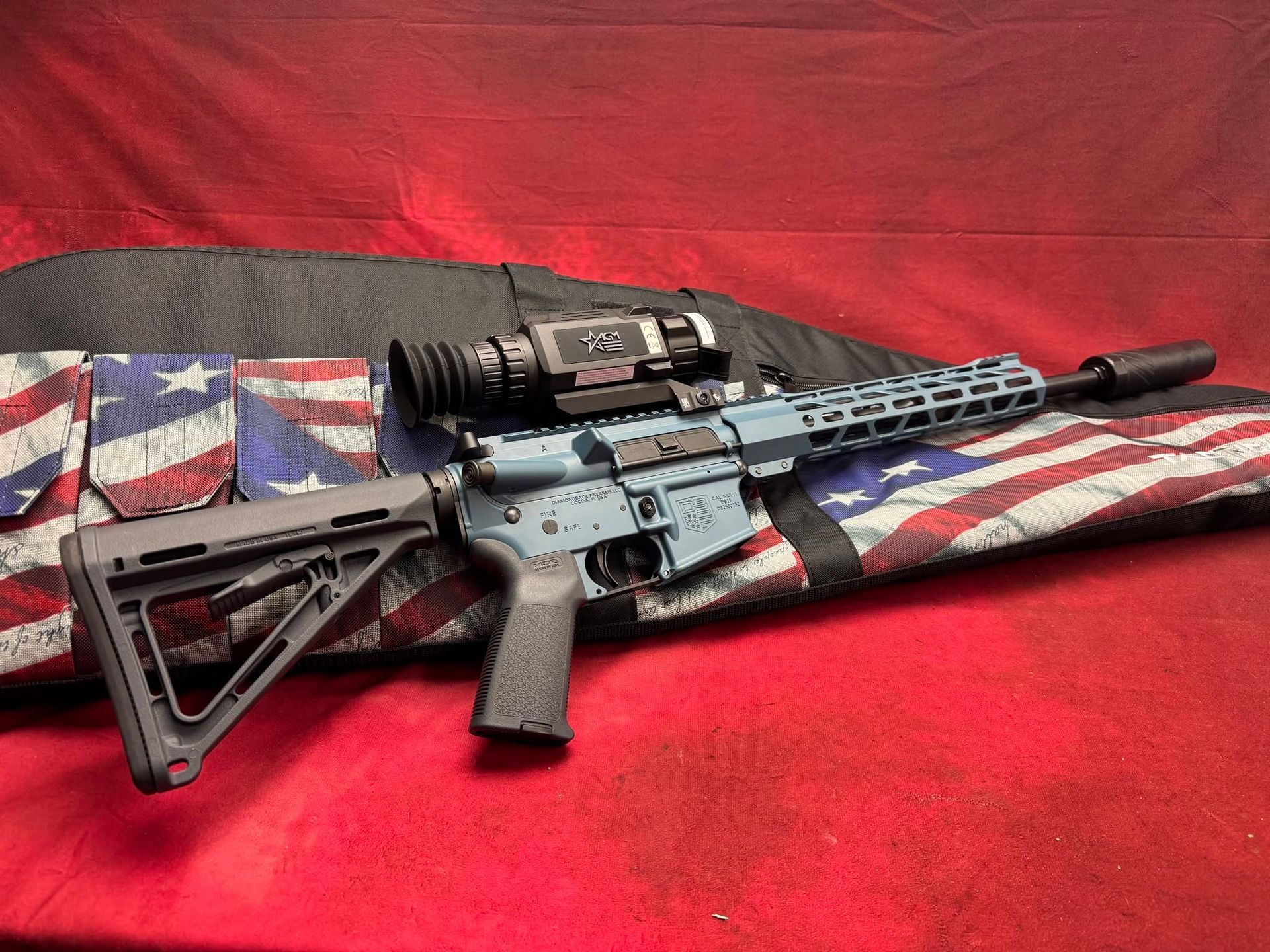 AR-style rifle with optic and adjustable stock on a red and Union Jack-patterned fabric background