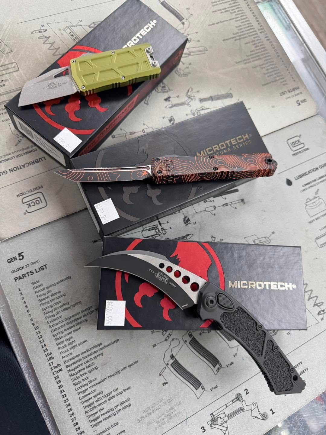 Three folding knives displayed on product boxes over a newspaper background