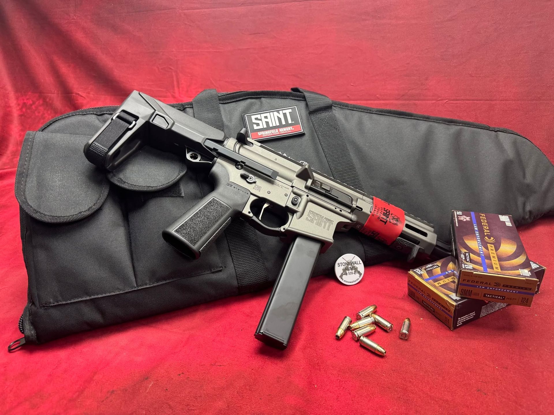 Black rifle with magazine and ammo on red cloth, alongside a soft gun case and ammo boxes.