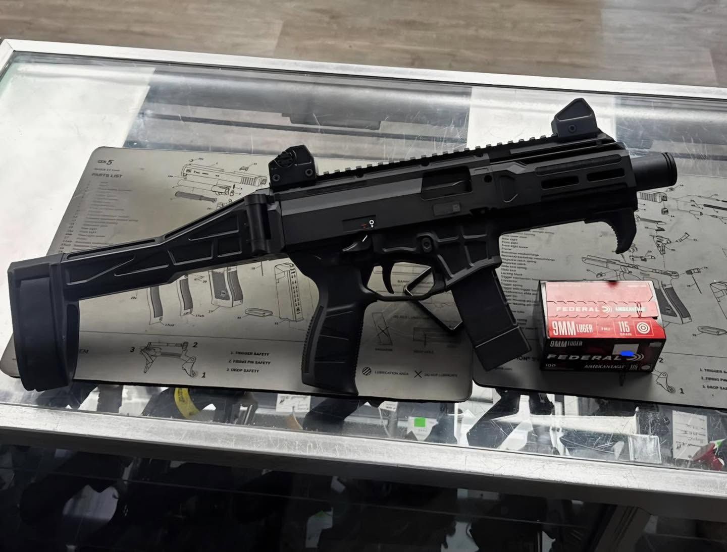 Black submachine gun with box of ammunition on a counter.