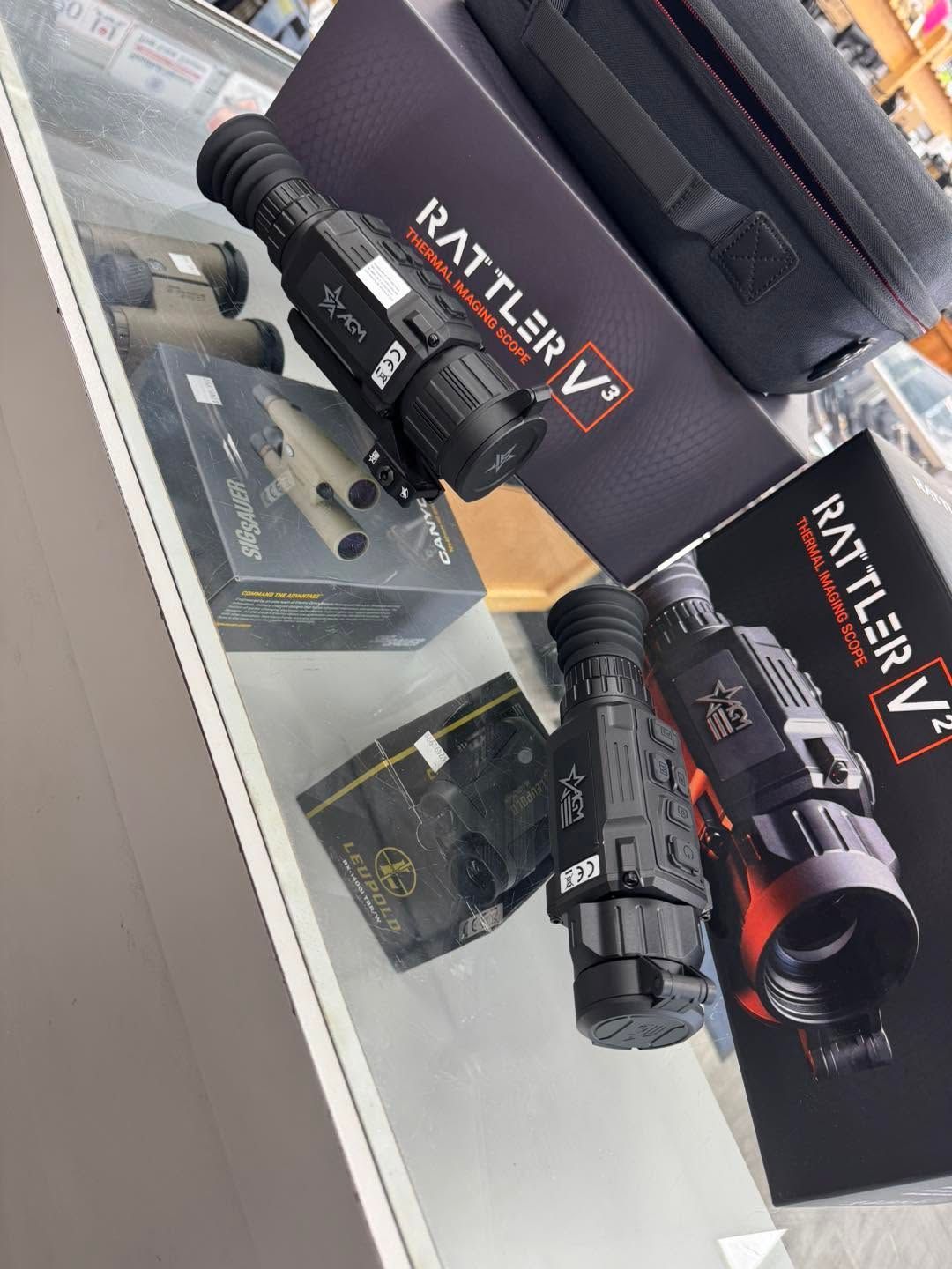 Two black Rattler V scopes on a store display, one with a red lens hood and one with a tan mount.