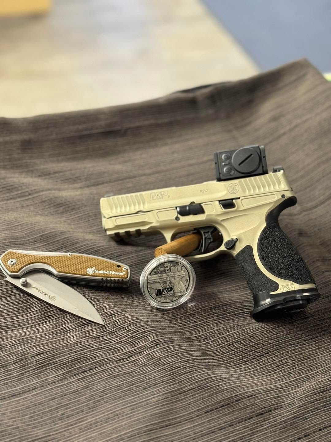 Handgun, folding knife, and wristwatch arranged on a fabric surface.