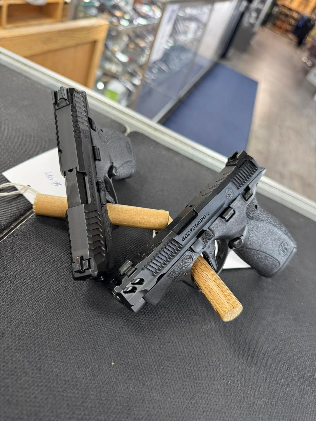 Two black pistols on display stands in a store, with tan grips and blurred background.