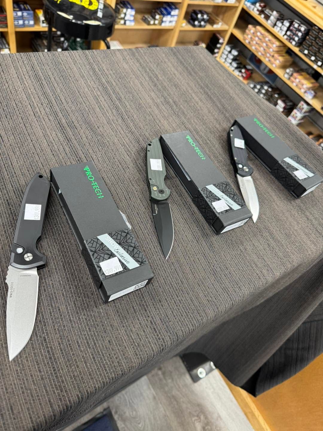 Four folding pocket knives displayed on a gray tablecloth in a store.