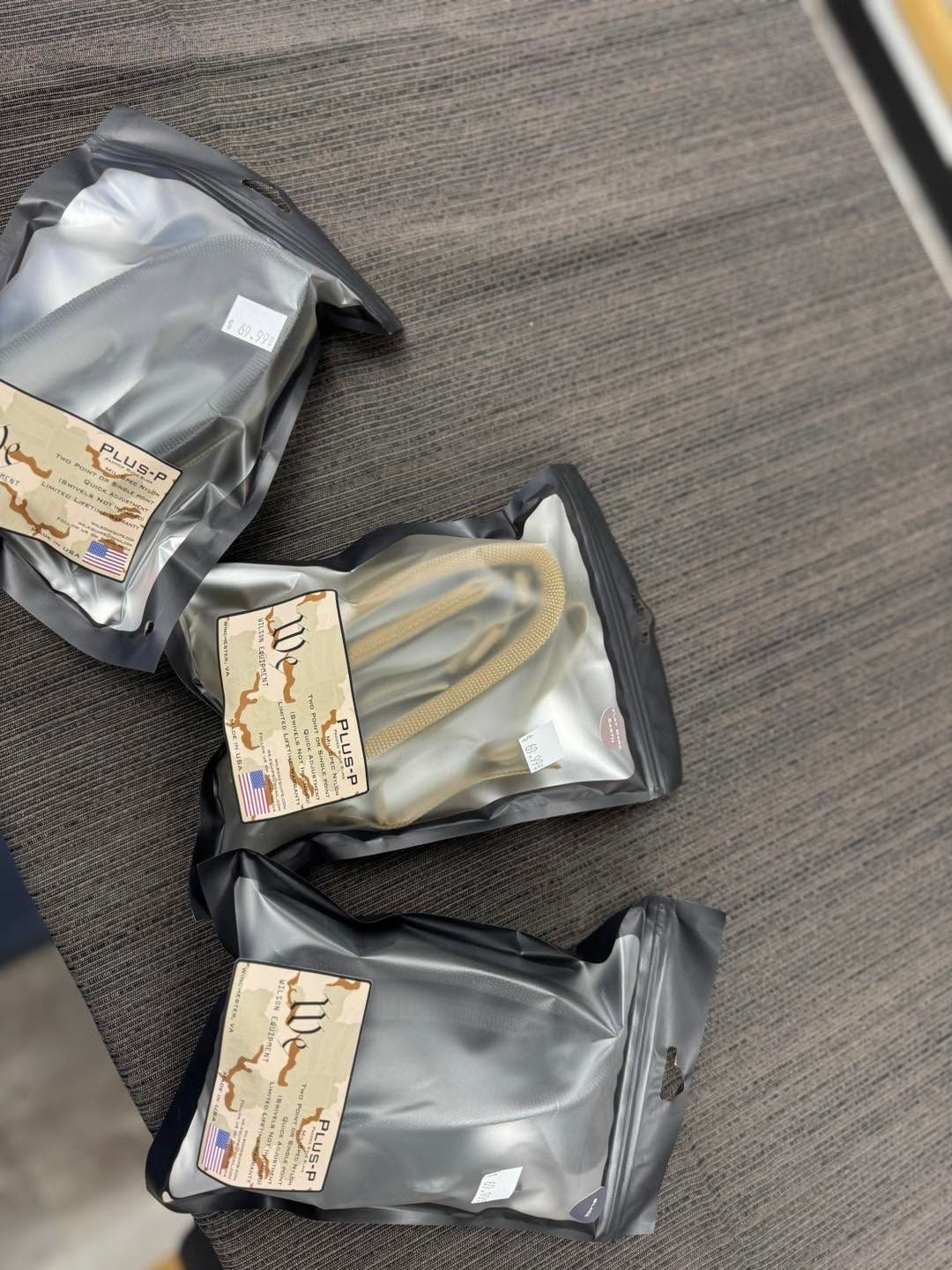 Three small silver pouches with paper labels lying on a gray carpet