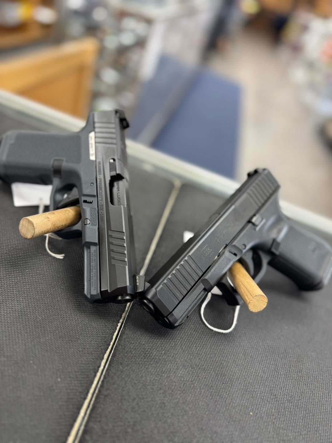 Two black handguns crossed on a counter, each with a tan cylindrical item in the magazine well