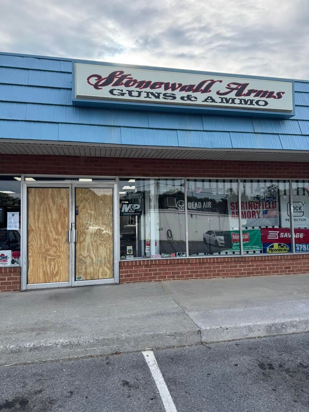 Storefront with boarded-up glass doors and a sign reading “Stonewall Arms Guns & Ammo.”
