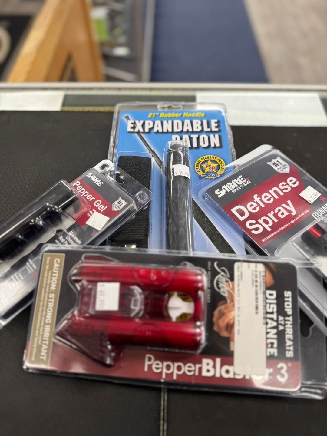 Assorted self-defense items in retail packaging, including pepper spray, a baton, and defense spray.