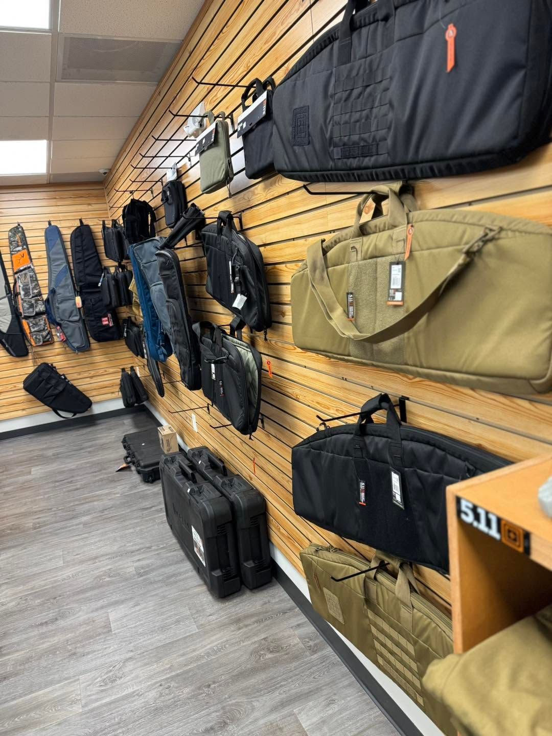 Tactical bags and cases displayed on slatwall in a store aisle, mostly black and tan.