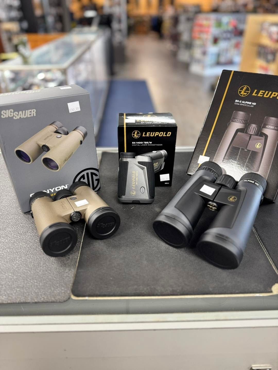 Binoculars displayed on a store counter, with boxed models in black, tan, and silver packaging.