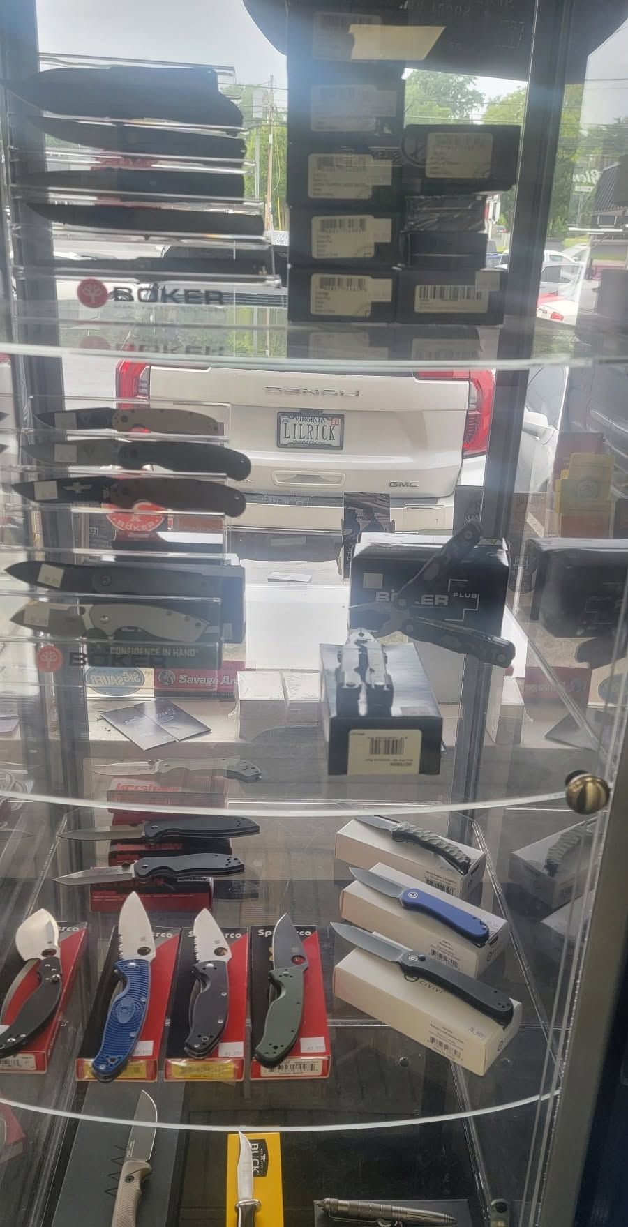Glass display case with assorted knives and multitools on shelves in a store.