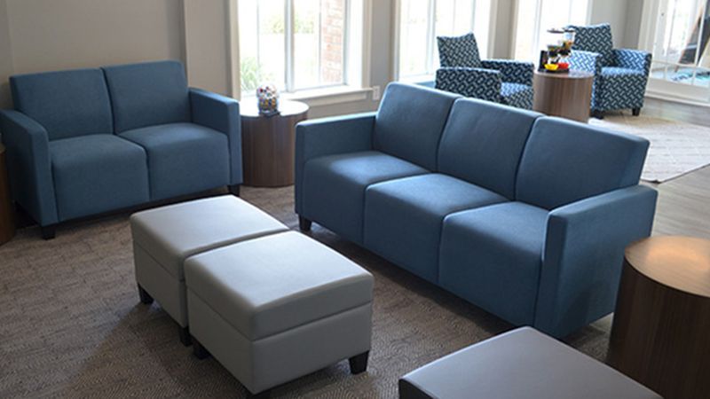 A living room with blue couches and white ottomans