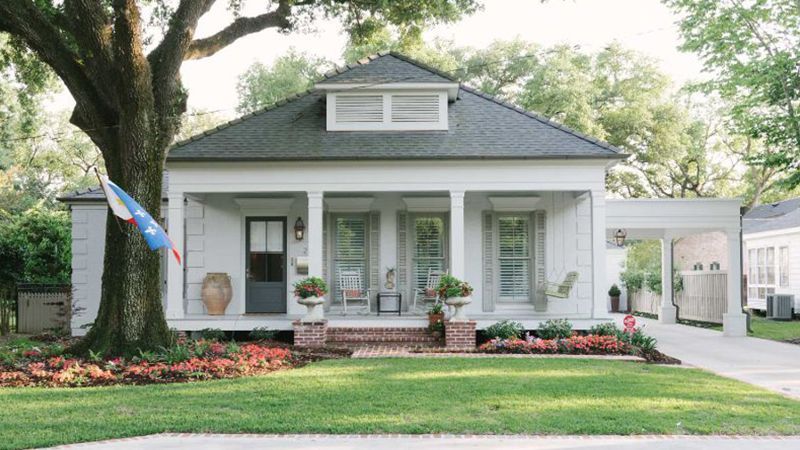 A white house with a porch and a tree in front of it.