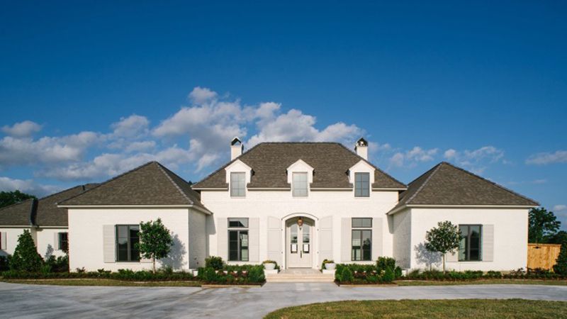 A large white house with a gray roof is sitting on top of a lush green field.