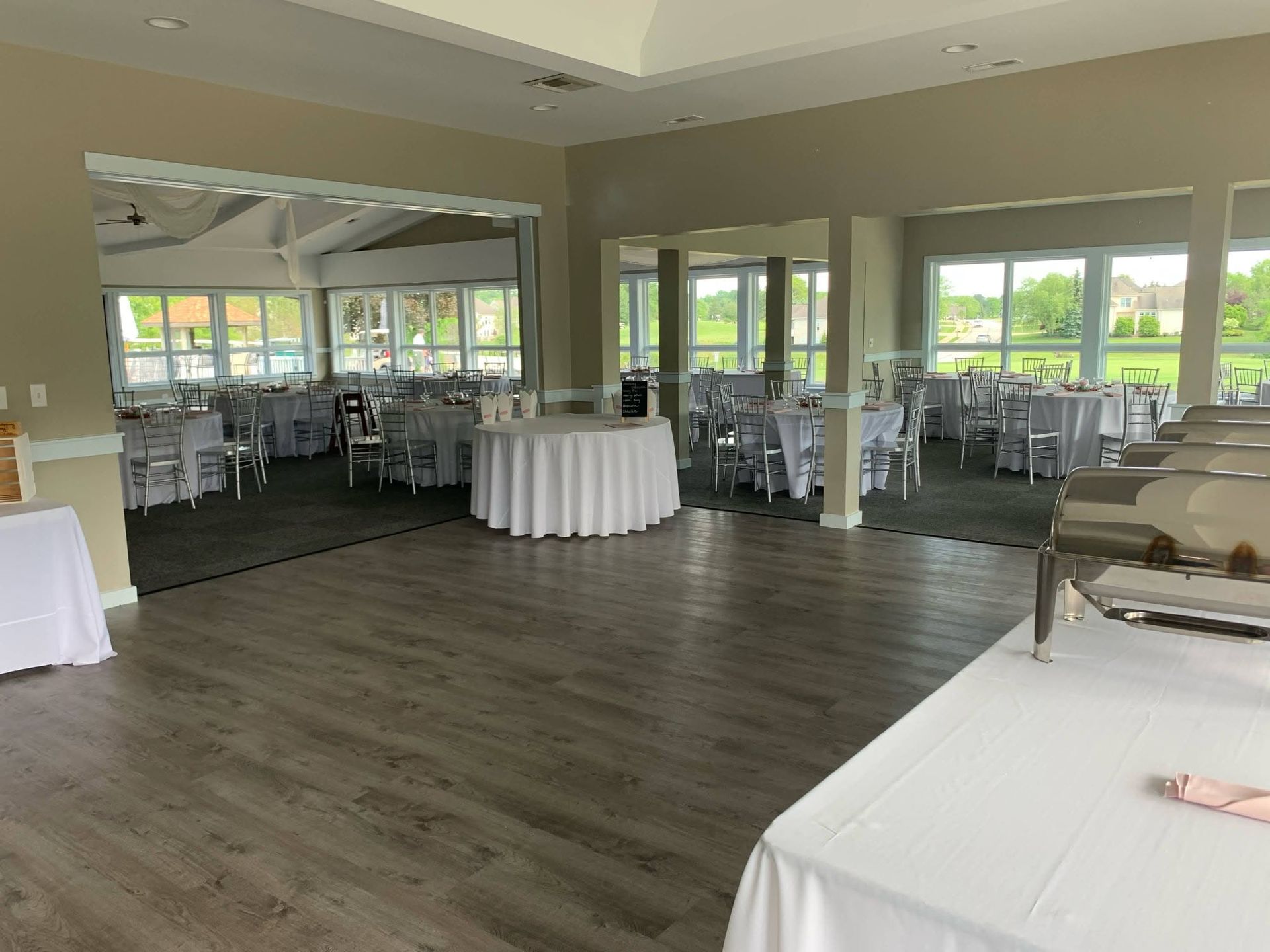 Banquet hall with round tables, white chairs, and buffet tables near large windows