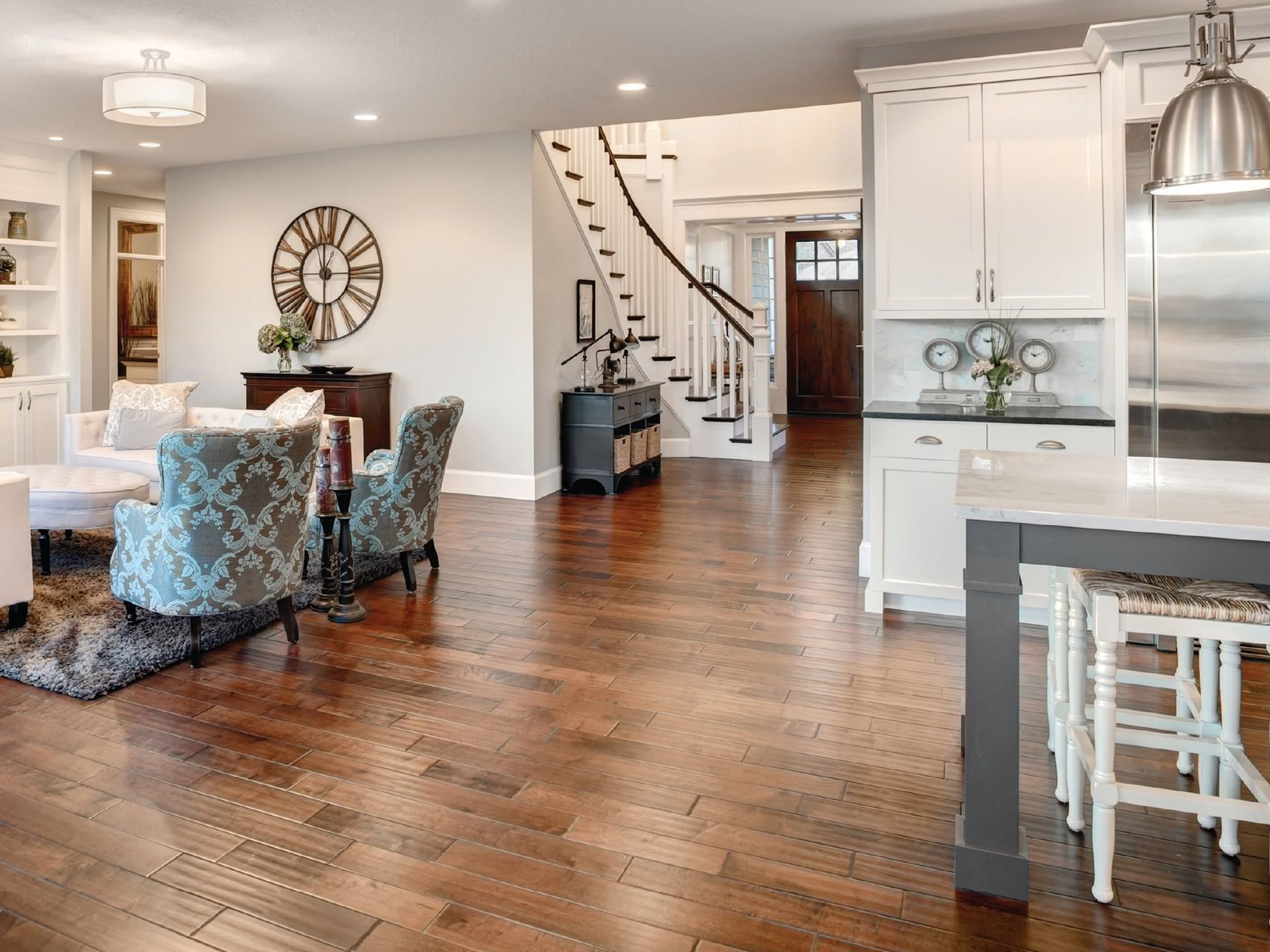 Bright open dining room and kitchen with hardwood floors, staircase, white cabinets, and blue patterned chairs