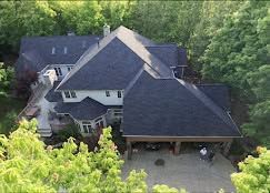 Aerial view of a large gray-roofed house surrounded by dense green trees