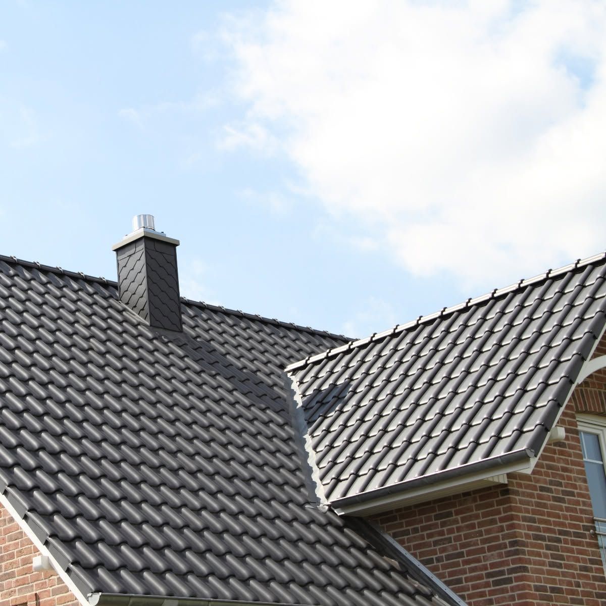 Two tiled house roofs with a brick chimney against a partly cloudy sky