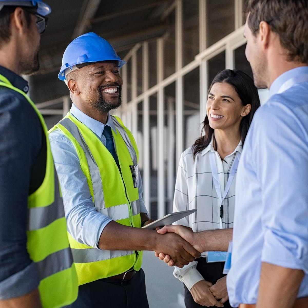 Construction team shaking hands at a job site, wearing hard hats and safety vests