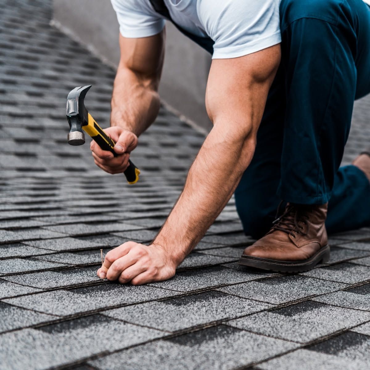 Worker hammering roof shingles during roof repair