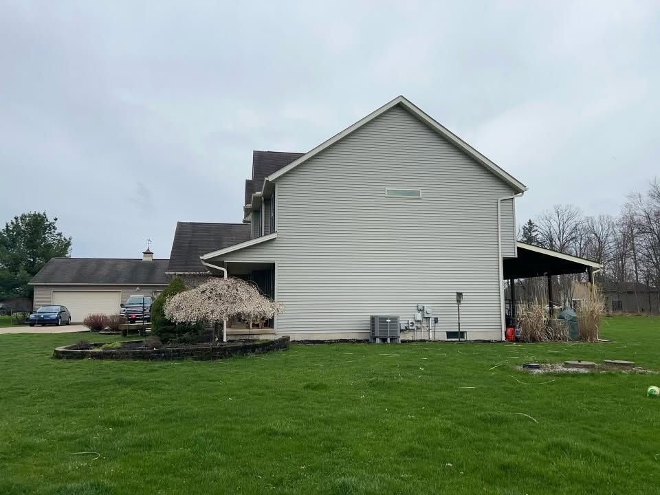White house with a green lawn and a small tree in a cloudy suburban yard