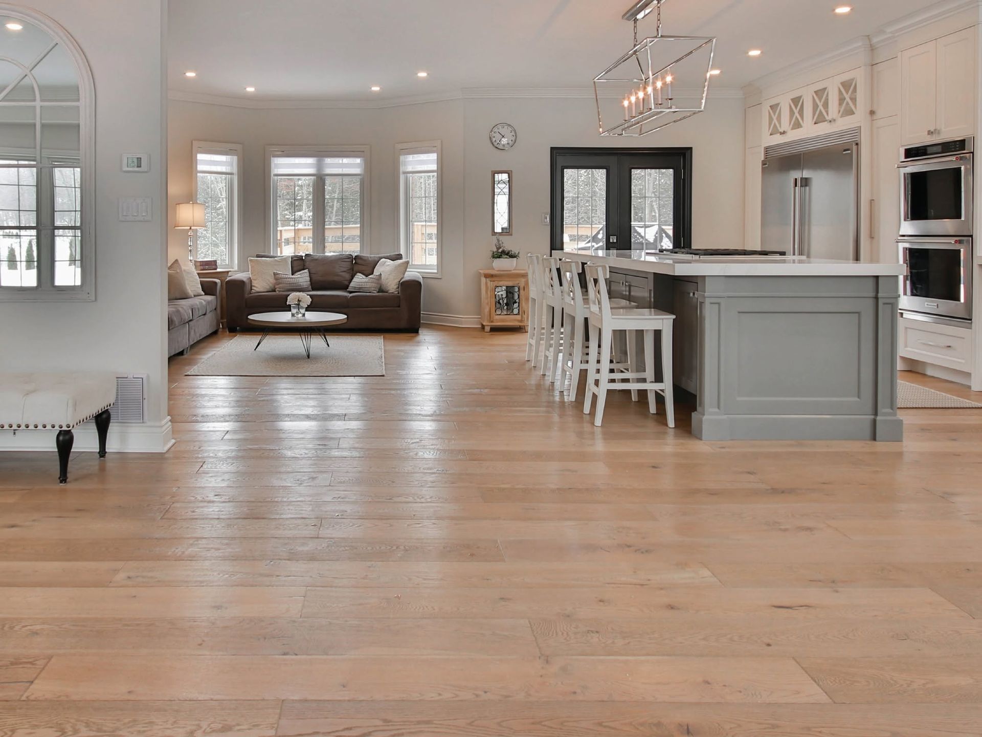 Bright open-concept living room with hardwood floors, gray furniture, and a kitchen island with barstools