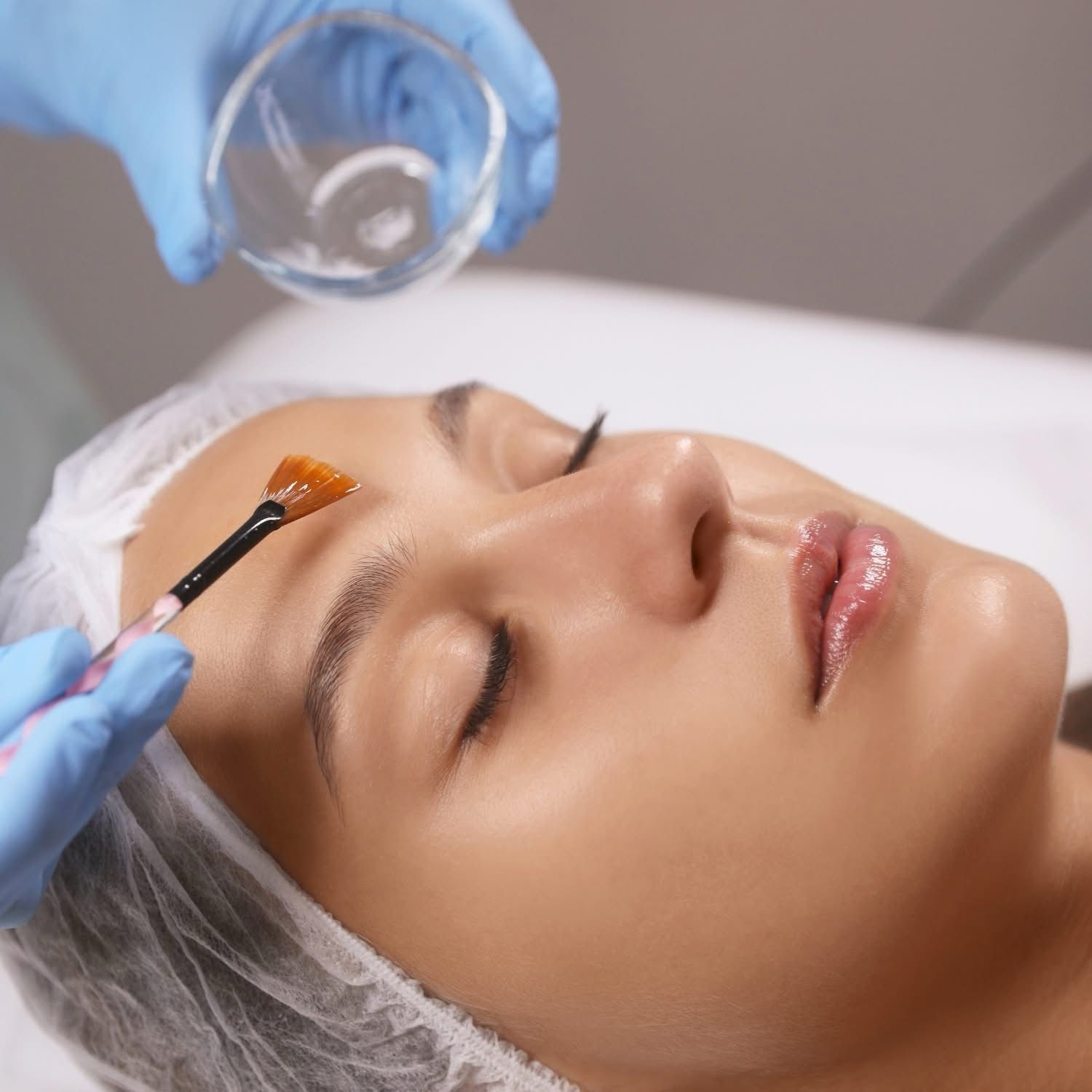 A woman is getting a facial treatment with a brush on her forehead.