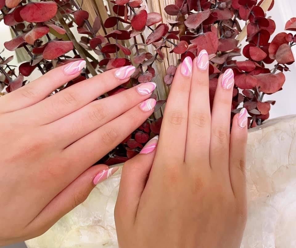 A close up of a woman 's hands with pink nails in front of a plant.