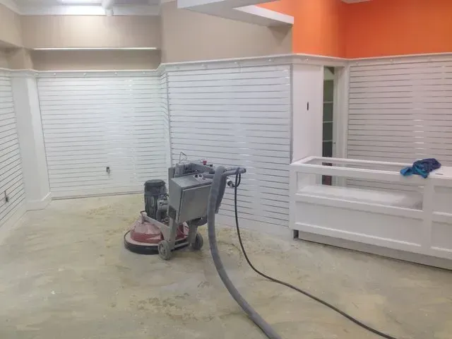 Floor grinder in a room, concrete floor, white slatted walls, orange accent, and white shelving.