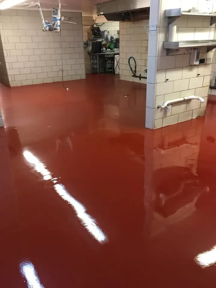 Red glossy floor in a kitchen with white tiled walls and stainless steel equipment.