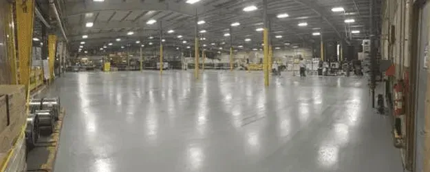 Inside of a large warehouse with a shiny gray floor. Several yellow pillars and ceiling lights are visible.