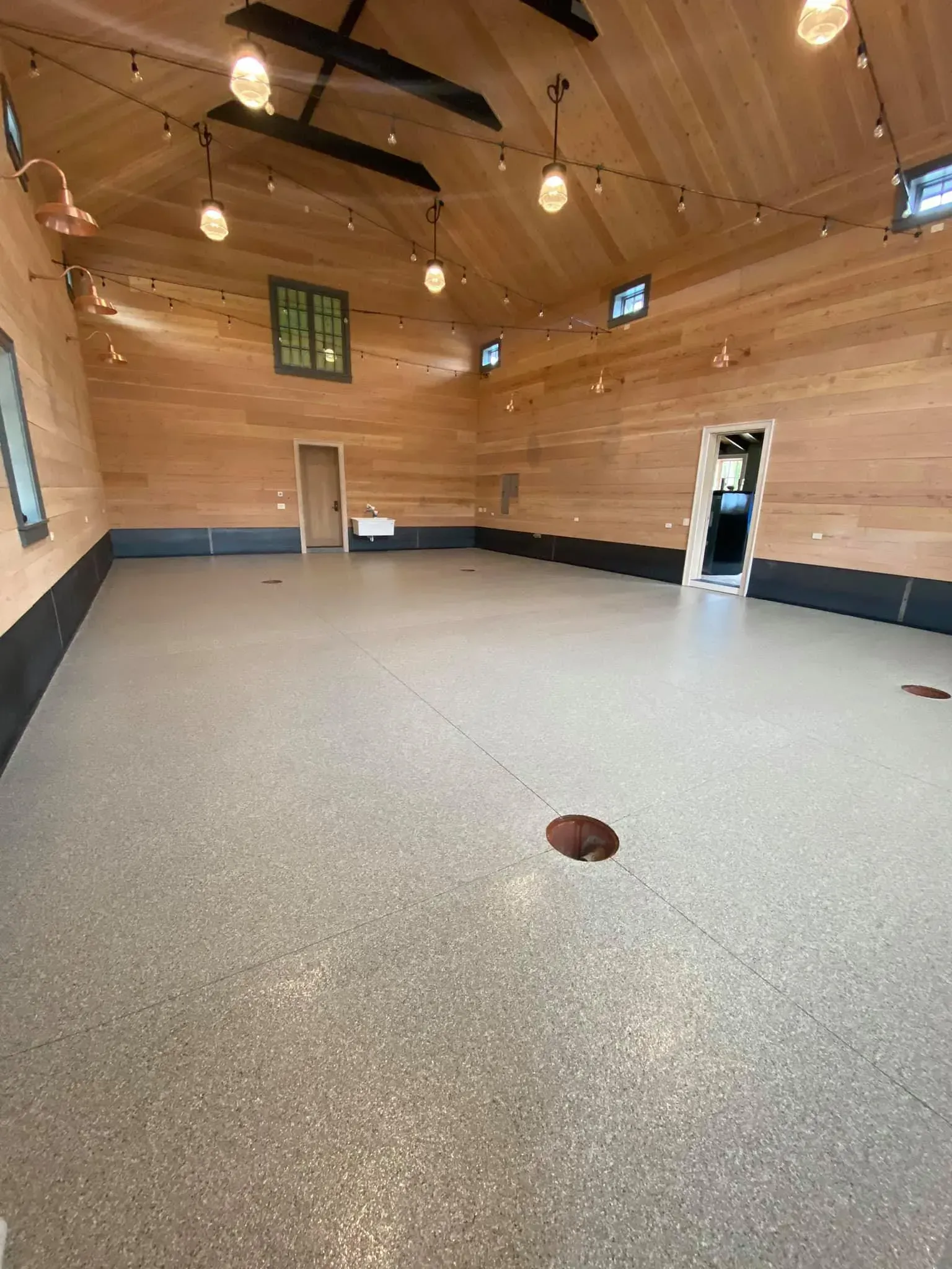 Empty room with wood paneling, string lights, gray floor, and a few doors.