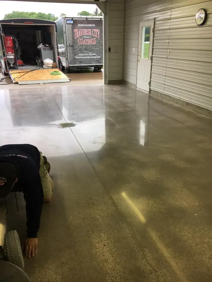 Person polishing a shiny concrete garage floor, open to a driveway with trailers.