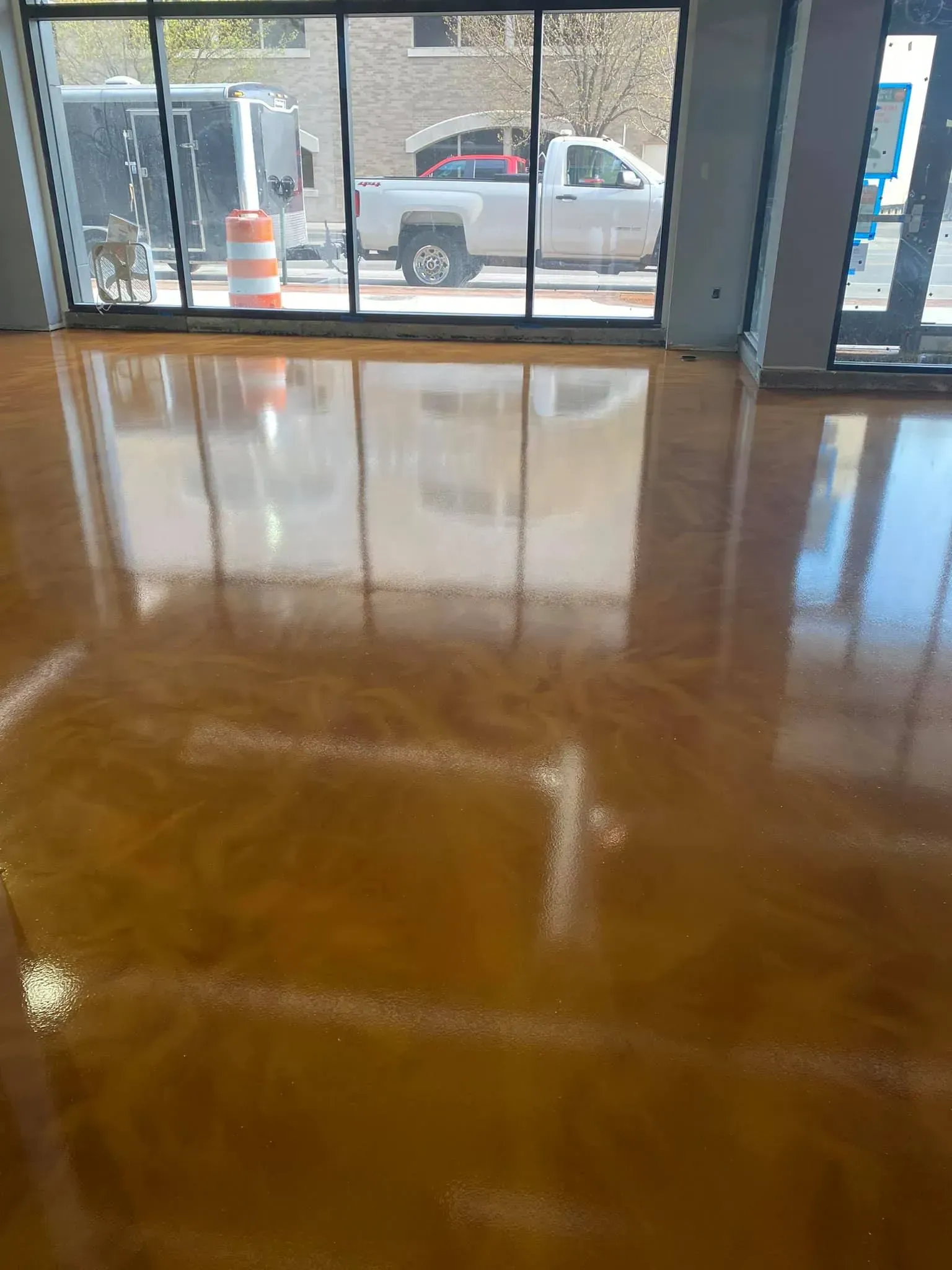 Shiny, golden-colored epoxy floor reflecting an outside view of a building with windows and a parked truck.