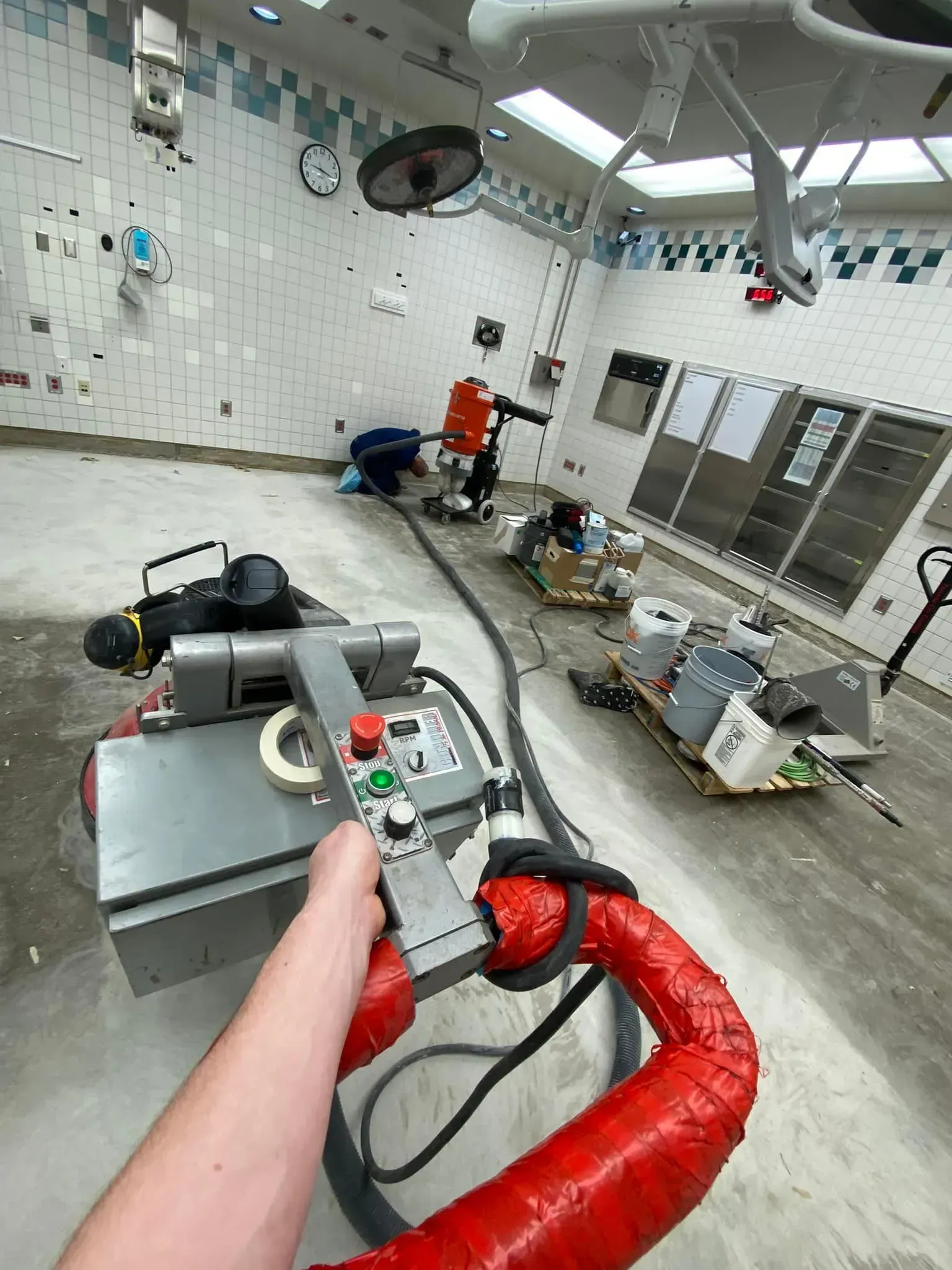 Person holding remote, operating equipment in a sterile room, possibly an operating room, with other machinery and tools.