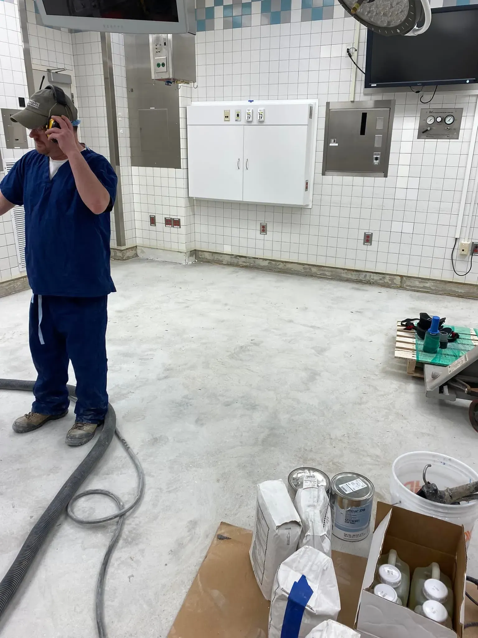 Person in blue scrubs in an operating room under renovation, with tools and materials on the floor.