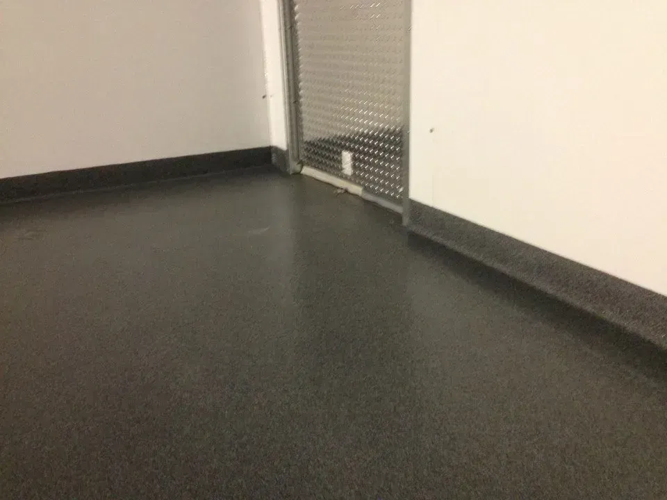 Black speckled floor meets white walls with black trim and a metal panel.